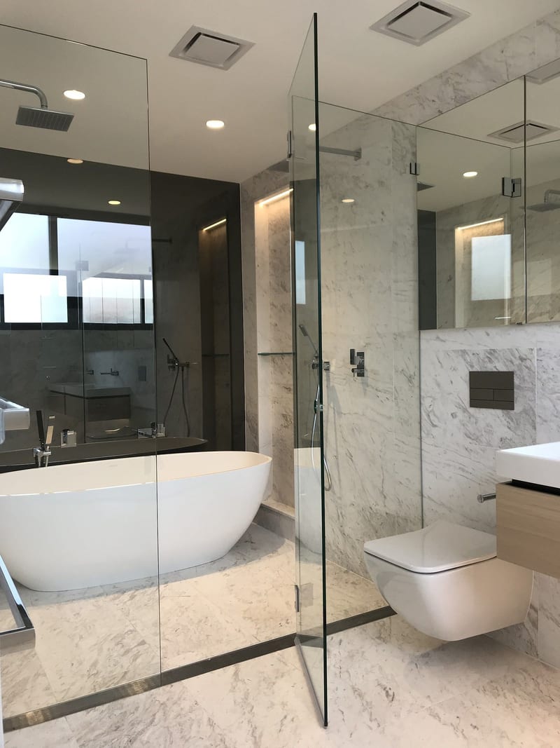 Floor-to-ceiling three panel inline frameless glass screen in a marble ensuite, with polished chrome hardware and a freestanding bath behind the glass